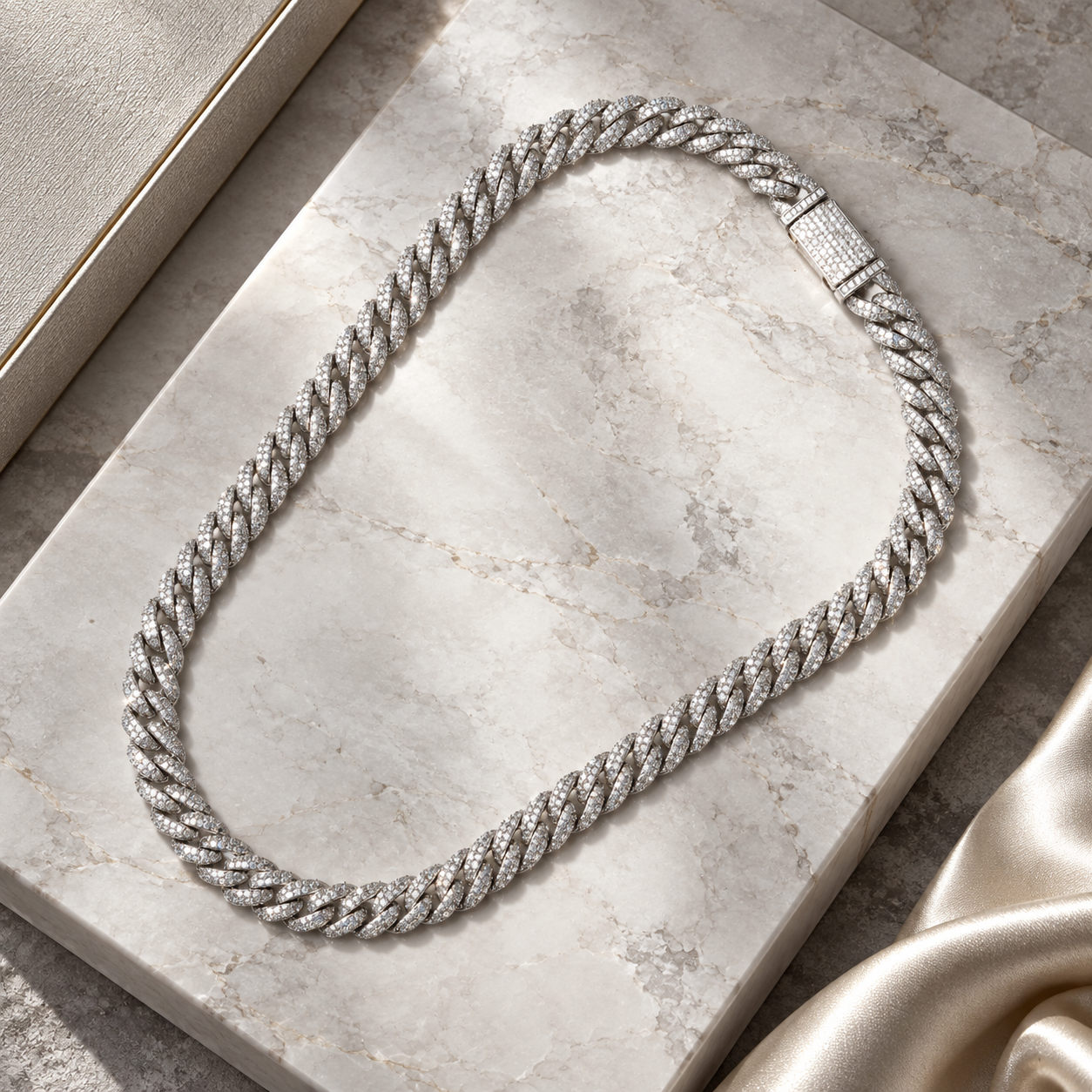 Silver-tone iced Cuban link chain laid on a marble slab with the pave clasp visible
